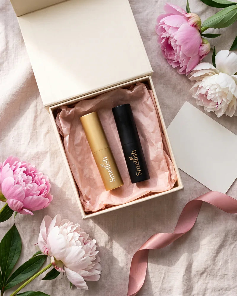 Open cadeaudoos met een gouden en een zwarte Smellish twist-up tussen roze pioenrozen