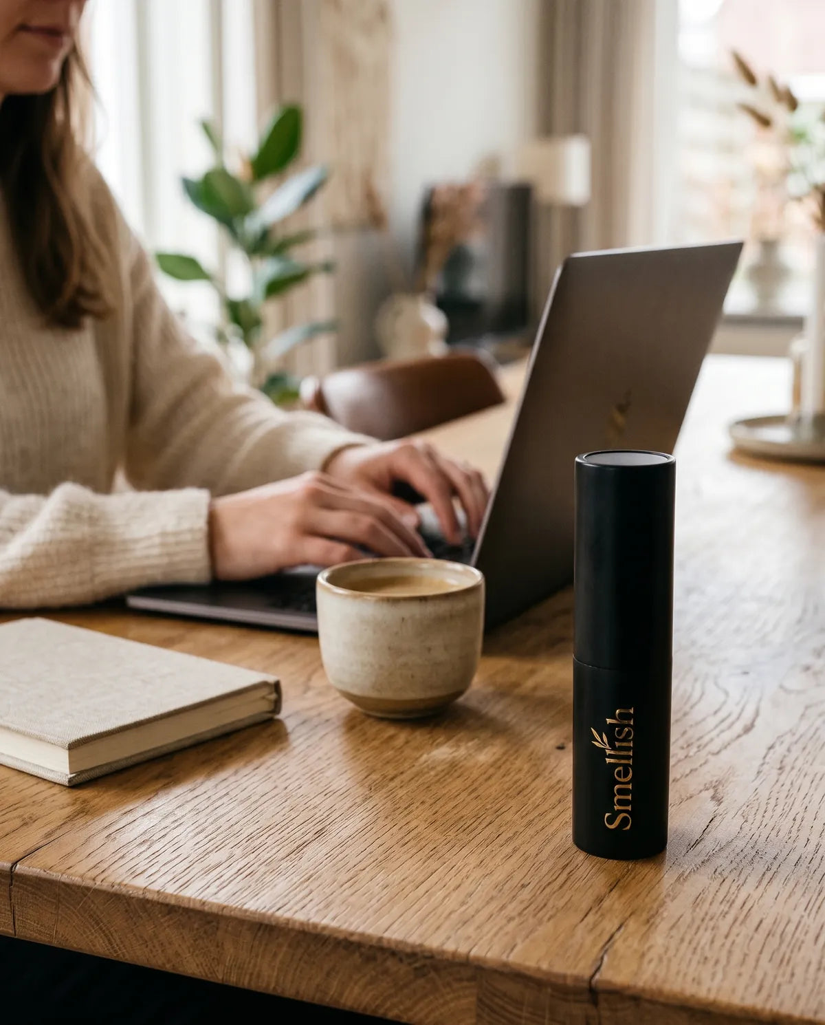 Zwarte twist-up travelspray op een eikenhouten tafel naast koffie, een notitieboek en een laptop